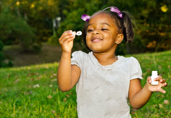Młoda dziewczyna afro-amerykańskich, grając z bąbelkami w parku — Zdjęcie stockowe