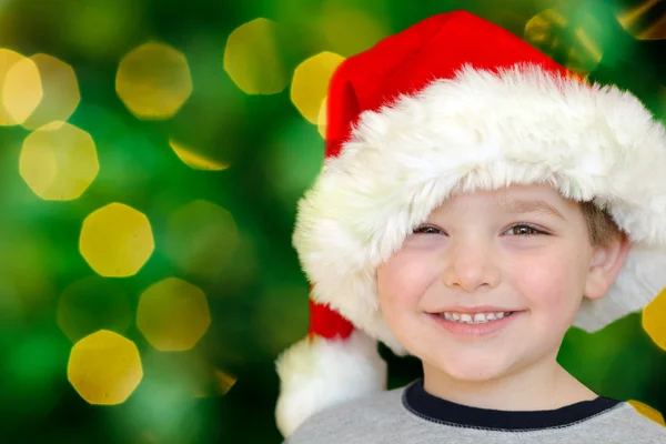 Portrait of young boy in Santa hat in front of Christmas tree — Stock Photo, Image