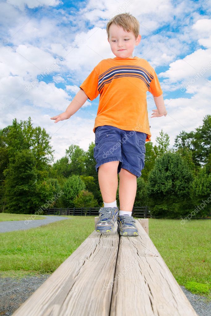 Young boy or kid balancing on beam obstacle on exercise trail outdoors at park