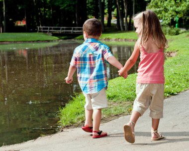 Hispanic girl and boy walk around pond. clipart