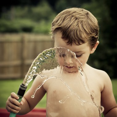 Boy or kid plays with water hose outdoors during summer or spring to cool off in hot weather clipart