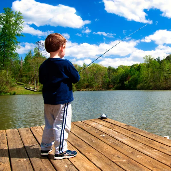 stock image Boy fishing from dock on lake.