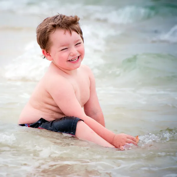 Ung pojke spelar i surf på stranden — Stockfoto