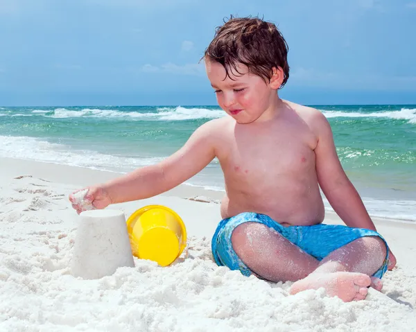 Young boy builds sand castle while playing on beach. — Stock Photo, Image