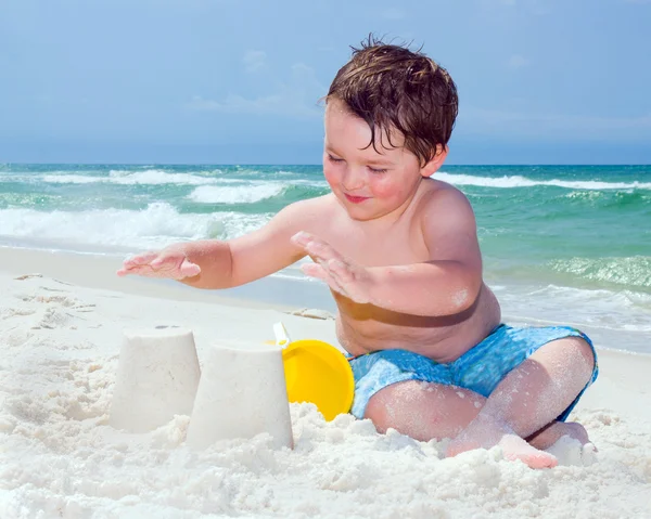 Young boy builds sand castle while playing on beach. — Stock Photo, Image