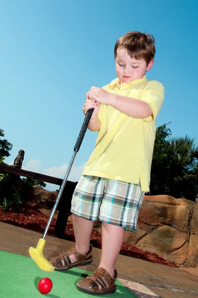 Ung pojke spelar minigolf på putt putt kurs. — Stockfoto