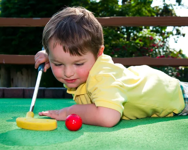 Młody chłopak gra minigolf na putt putt course. — Zdjęcie stockowe