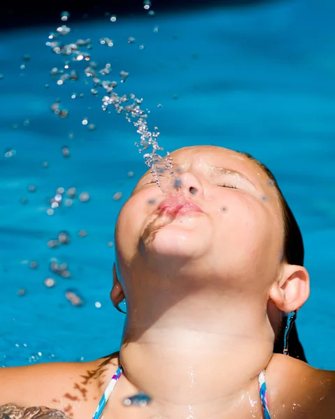 Flicka blåser ett vatten pip när du simmar i poolen. — Stockfoto