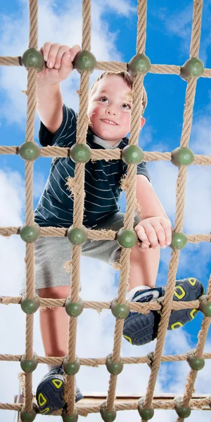 Jovem menino escalando obstáculo corda no parque infantil — Fotografia de Stock