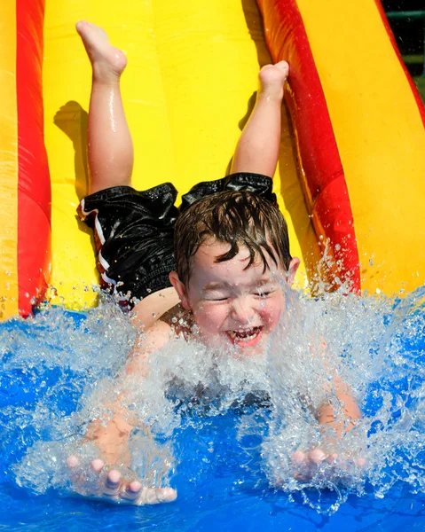 Young boy or kid has fun splashing into pool after going down water slide during summer — Stock Photo, Image