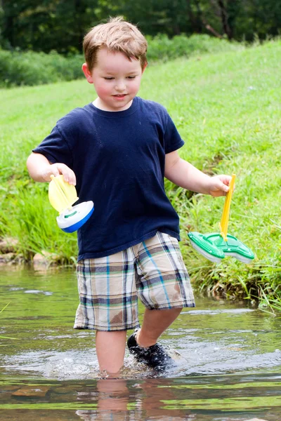 Chico se divierte jugando con barcos de juguete en arroyo en el parque durante la primavera o el verano — Foto de Stock
