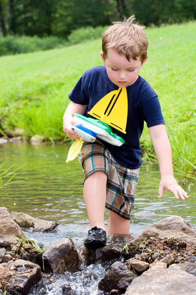 Pojken har roligt genom att spela med leksak båtar i creek Park under våren eller sommaren — Stockfoto