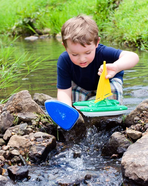 Boy has fun by playing with toy boats in creek at park during spring or summer — Stock Photo, Image