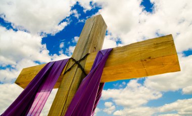 Cross with purple drape or sash for Easter with blue sky and clouds in background clipart
