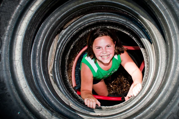 Girl plays in recycled tire tunnel at playground. — Stock Photo, Image
