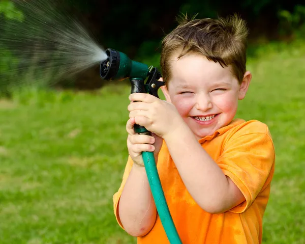 Ребенок играет с водяным шлангом на открытом воздухе летом или весной, чтобы охладить в жаркую погоду — стоковое фото