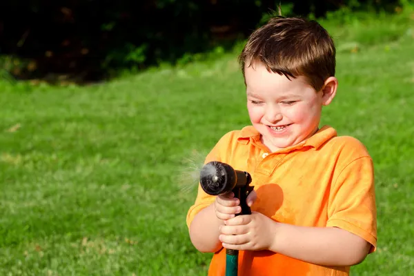 Kind spielt im Sommer oder Frühling im Freien mit Wasserschlauch, um sich bei heißem Wetter abzukühlen — Stockfoto
