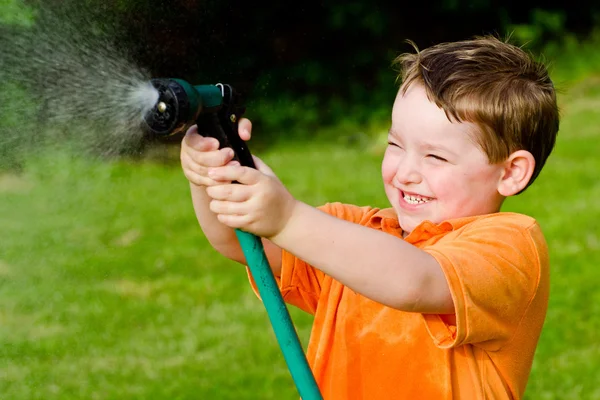 Child plays with water hose outdoors during summer or spring to cool off in hot weather — Stock Photo, Image