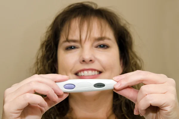 Close up of positive pregnancy test with happy, smiling middle-aged woman in background — Stock Photo, Image