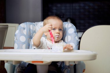 Baby boy eating yoghurt cream clipart