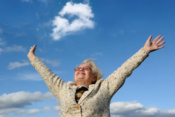 Счастливая пожилая леди с протянутыми руками на фоне голубого неба — стоковое фото