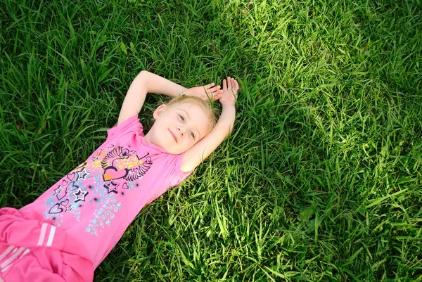 Молодая девушка в розовом лежит на зеленой траве — стоковое фото