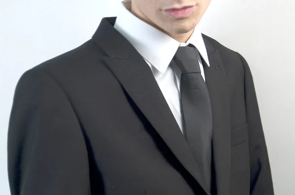 Junger hübscher Geschäftsmann im schwarzen Anzug auf weißem Grund. — Stockfoto