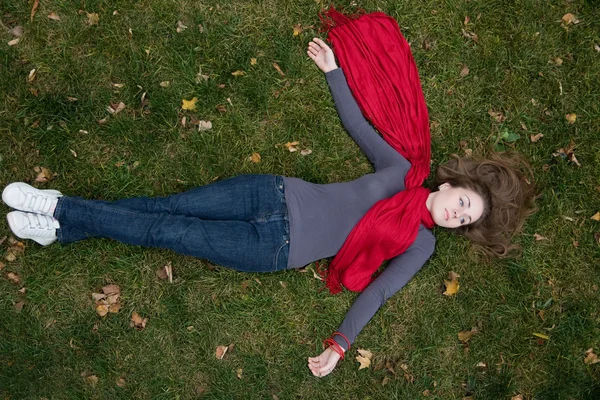 Brunette mooie vrouw is in rode sjaal liggen op het gras. — Stockfoto
