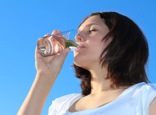 Mujer joven bebiendo agua en el cielo fondo — Foto de Stock