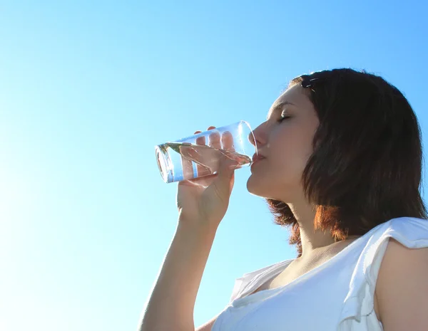 Mladá žena pitné vody na pozadí oblohy — Stock fotografie