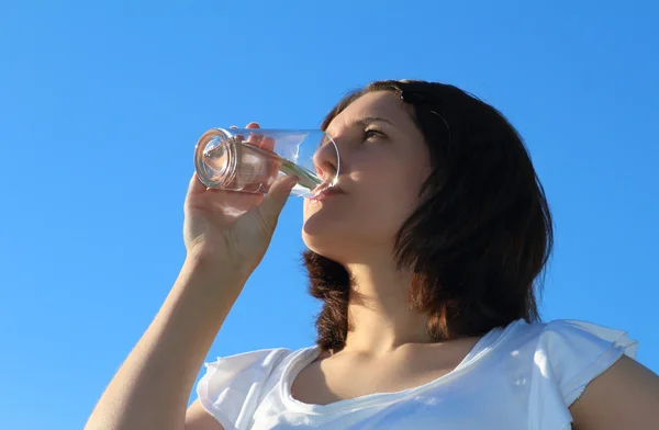 Jonge vrouw drinken van water op hemelachtergrond — Stockfoto