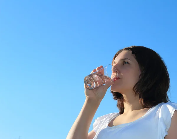 Young woman drinking water on sky background — Stock Photo, Image