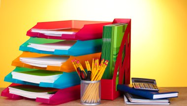 Bright paper trays and stationery on wooden table on yellow background clipart