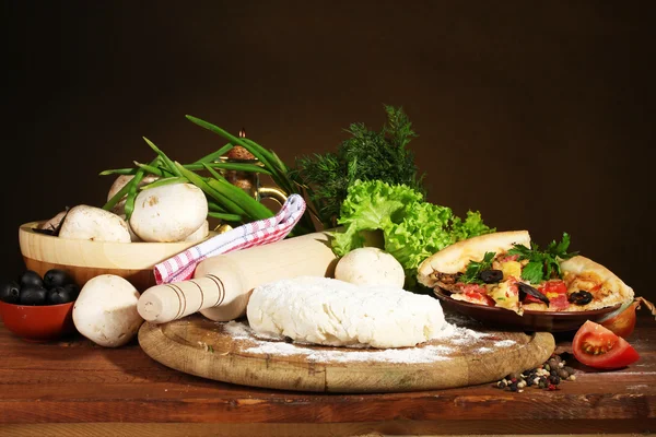 Leckerer Pizzateig, Gewürze und Gemüse auf Holztisch auf braunem Hintergrund — Stockfoto