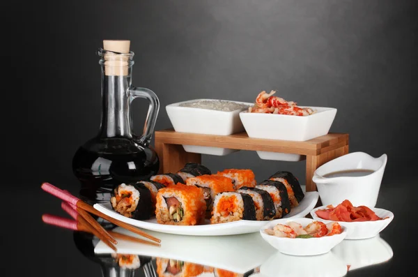 Pyszne sushi na płytkę, pałeczki, sos sojowy, ryby i krewetki na szarym tle — Zdjęcie stockowe