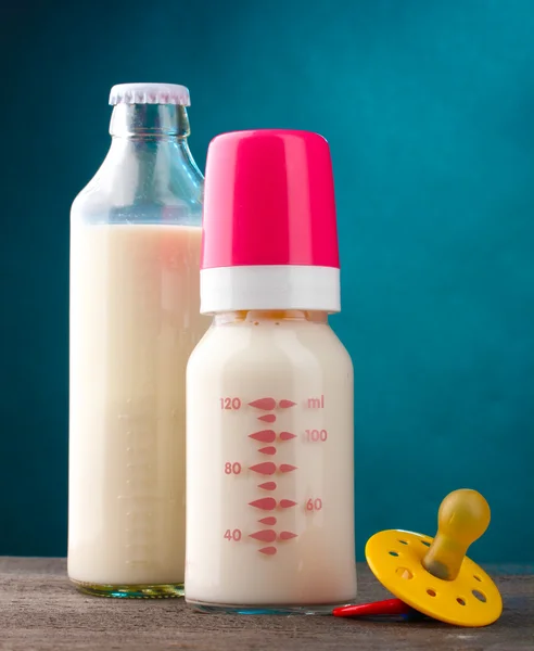 Butelki mleka i smoczek na drewnianym stole na niebieskim tle — Zdjęcie stockowe