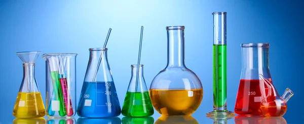 Vidros de laboratório diferentes com líquido de cor e com reflexão sobre fundo azul — Fotografia de Stock