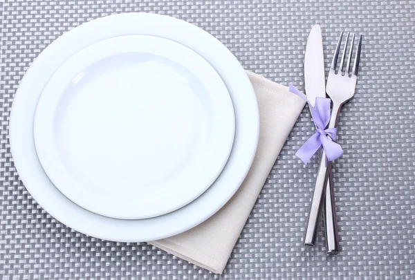 Білі порожні тарілки з виделкою і ножем пов'язані стрічкою на сірій скатертині — стокове фото