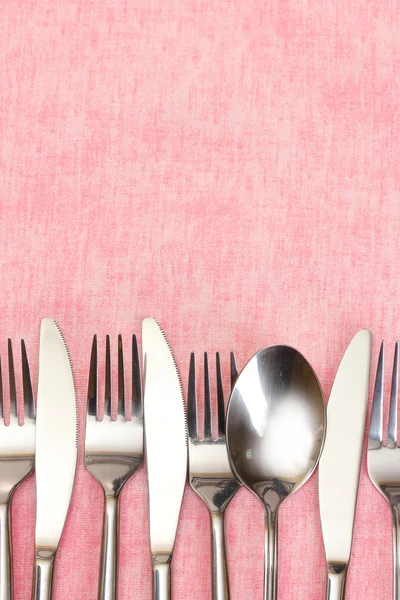 Forchette, cucchiai e coltelli su una tovaglia rosa — Foto Stock