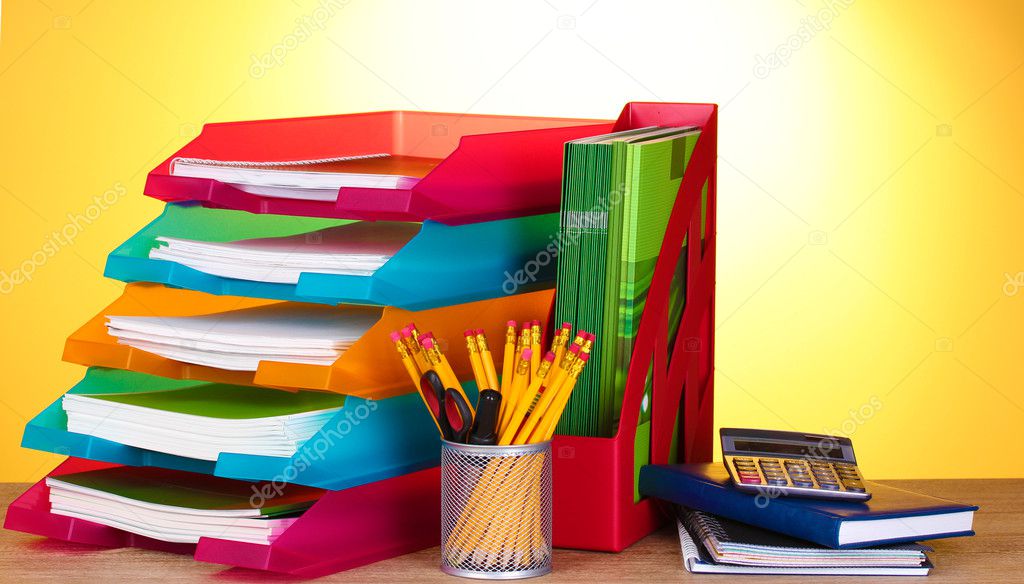 Bright paper trays and stationery on wooden table on yellow background