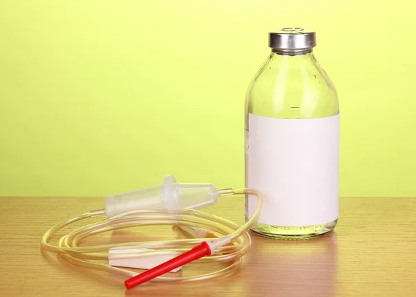 Botol antibiotik intravena dan infus plastik diletakkan di atas meja kayu dengan latar belakang hijau — Stok Foto