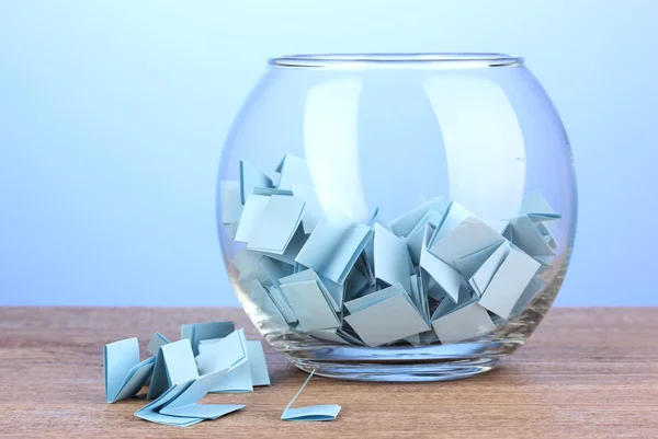 Bitar av papper för lotteri i vas på träbord på blå bakgrund — Stockfoto