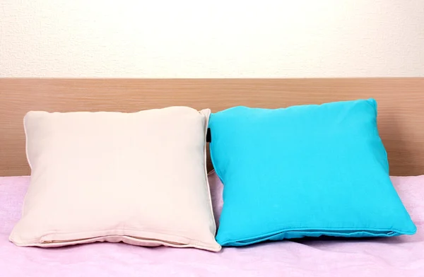 Světlé polštáře na posteli na béžové pozadí — Stock fotografie