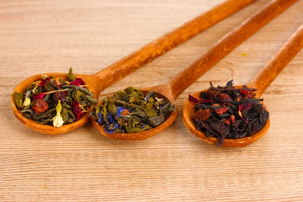 Olika typer av grönt och svart torka te i skedar på träbord — Stockfoto