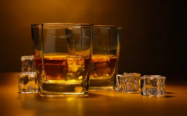 Dwie szklaneczki szkockiej whisky i lodu na drewnianym stole na brązowym tle — Zdjęcie stockowe