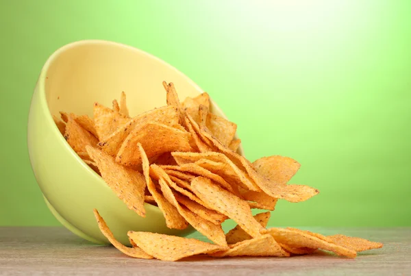 Tasty potato chips in green bowl on wooden table on green background — Stock Photo, Image