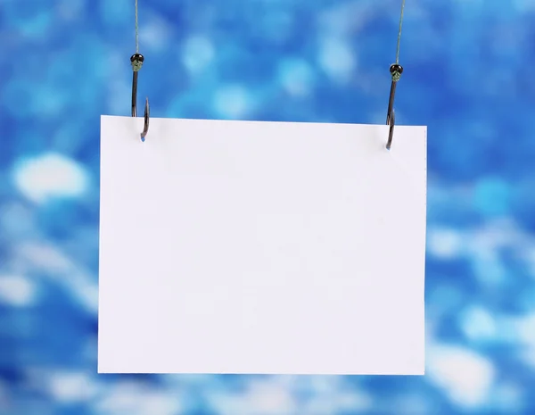 Empty sheet of a paper on fish hooks on blue background — Stock Photo, Image
