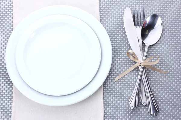 Assiettes blanches vides avec fourchette, cuillère et couteau attachées avec un ruban sur une nappe grise — Photo