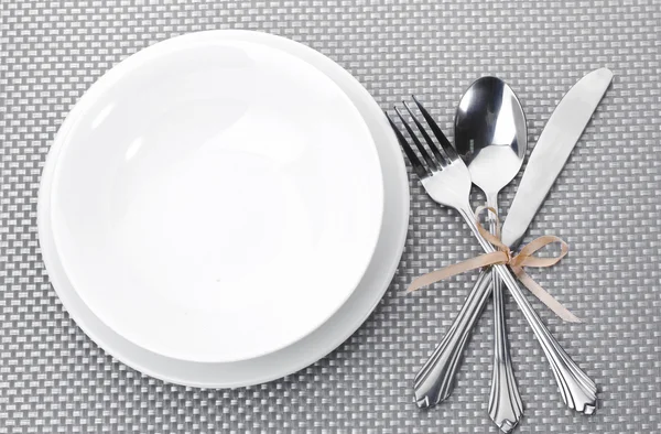 Білі порожні тарілки з виделкою, ложкою і ножем пов'язані стрічкою на сірій скатертині — стокове фото