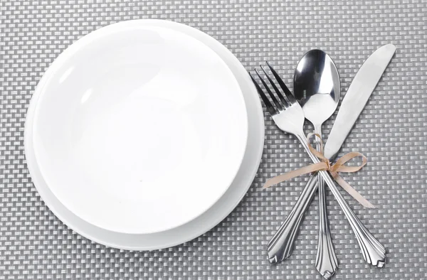 Platos blancos vacíos con tenedor, cuchara y cuchillo atados con una cinta sobre un mantel gris —  Fotos de Stock